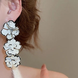 Detail view of triple white flower drop earrings with black edges on a model