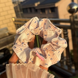 Close-up of pink and white striped fabric scrunchie with blue polka dot embroidery detail