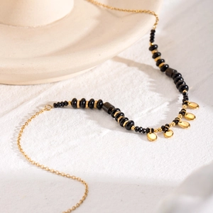Elegant gold necklace featuring black crystal beads and circular metal charms on textured surface