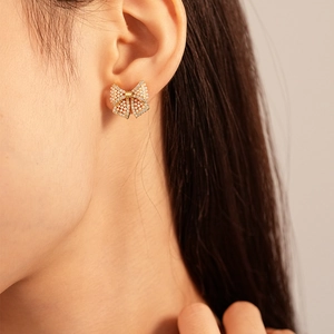 Detail view of dainty gold bow earrings with pearls and zircons worn on model ear
