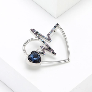 Detailed view of silver heart brooch with blue gemstone and violet rhinestones
