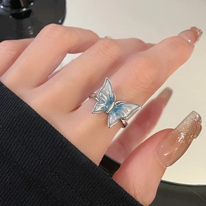 Macro detail of a silver open ring featuring blue enamel butterfly and pleated texture