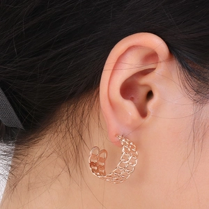 Detail of vintage hollow chain-style gold earrings worn on ear with metallic texture