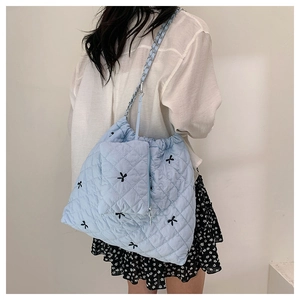 Detail of light blue quilted tote bag with black bow embroidery and metal chain strap