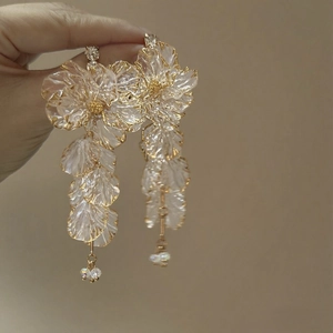 Detailed close-up of white translucent flower earrings with golden beads and long tassels