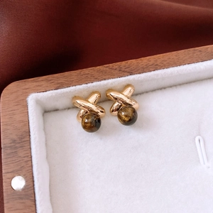 Macro detail of 18k gold plated X-shaped tiger eye stud earrings in a wooden jewelry box
