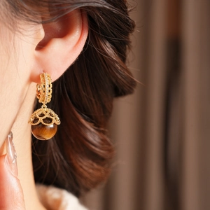 Detail of vintage gold-plated hoop earrings with tiger eye stone and intricate filigree