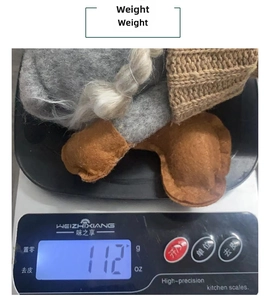 Close-up of a festive knitted Christmas gnome gnome being weighed on a scale at 112 grams