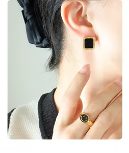 Detail of Roman numeral square studs and a black smiley ring in 18K gold finish