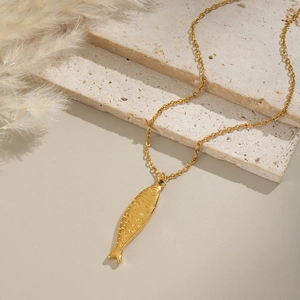 Détail du collier avec pendentif poisson doré sur pierre travertin et décor de roseau