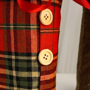 Detailed macro view of plaid Christmas wine bottle cover with red ribbon and wood buttons