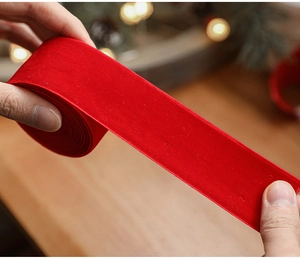 Close-up of hands holding red velvet Christmas ribbon with white stitched edges