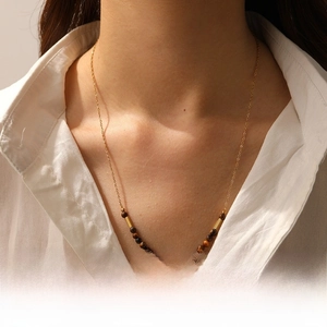Detail of tiger eye beads and gold bar links on a multilayered pearl stainless steel necklace