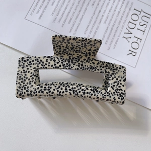Detail view of a large rectangular acetate hair claw clip with black and white speckle pattern
