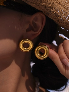 Close-up of polished gold hollow hoop earrings worn by a model in warm natural light