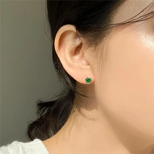 Close-up of heart-shaped emerald green zircon stud earrings worn on a female ear