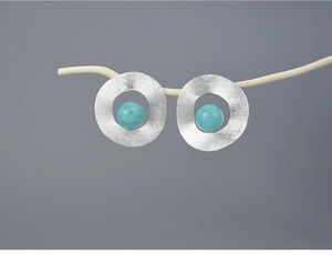 Close-up of geometric S925 silver stud earring with blue stone on a minimalist branch