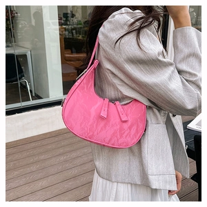 Detailed view of a pink pleated crescent underarm bag worn by a model in a modern outdoor setting