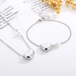 Détail du pendentif haricot argenté et perle blanche sur collier et bracelet