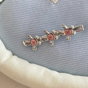 Detailed view of silver metal hairpin with three pink rhinestone flowers on blue cloth