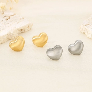 Détails des boucles d'oreilles cœur mates en or et argent sur un support en pierre