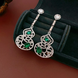 Macro shot of hollow gourd earrings with green gemstones and silver metal on velvet box