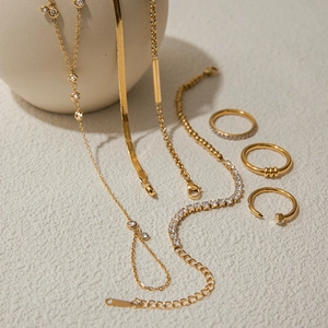 Elegant gold stainless steel jewelry set including necklaces and rings on textured surface