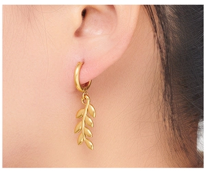 Close-up of golden wheat leaf pendant earring worn to show texture and polish