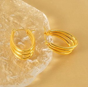 Macro view of 18k gold triple layered hoop earrings on warm gold satin and glass