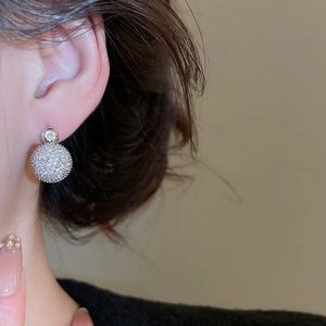 Close-up of sparkling silver zircon pavé ball earrings worn on ear with minimalist style