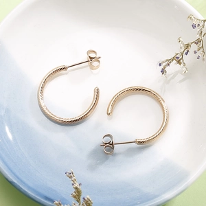 Macro shot of gold-plated twisted C-shape hoop earrings on a decorative ceramic tray