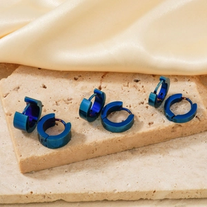 Macro shot of three pairs of deep blue titanium steel huggie earrings on stone
