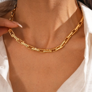 Close-up of golden geometric chain necklace worn by a model in a white shirt