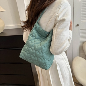 Stylish green quilted tote bag with heart patterns for women in a casual indoor setting