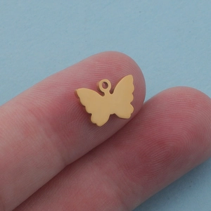 Minimalist golden stainless steel butterfly pendant shown on a finger for scale