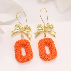 Detail of orange rose-embossed oval pendant earrings with golden ribbon bow accents