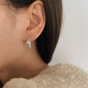 Close-up of minimalist silver knot stud earrings worn by a model in a high-fashion shot