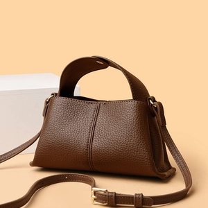 Minimalist square dark brown leather handbag with adjustable strap on neutral background