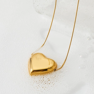 Polished gold hollow heart pendant necklace with fine snake chain over water droplets