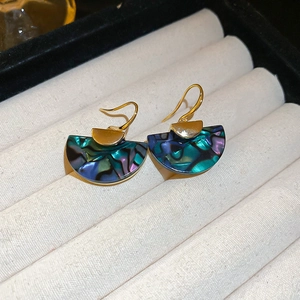Macro shot of fan-shaped abalone shell earrings with golden hooks on beige velvet