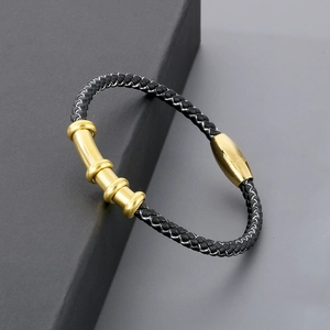 Detail of black braided leather bracelet with golden metal tubes and magnetic clasp