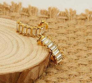 Macro shot of gold U-shaped earrings with baguette-cut zircon stones on wood