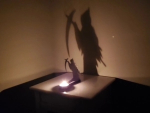 Grim Reaper silhouette candle holder casting a large spooky shadow on the wall
