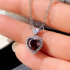 Close-up of heart-shaped red gemstone pendant with silver chain and halo diamonds