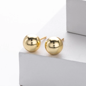 Close-up of polished gold spherical stud earrings on a white minimalist display stand
