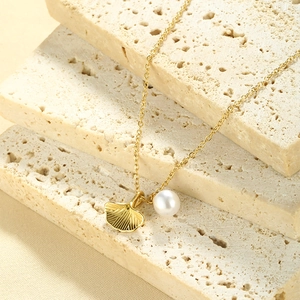 Detail of a gold ginkgo leaf necklace with a white pearl on a natural stone background