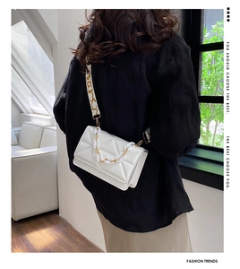 Detailed shot of white quilted crossbody bag with stylish chain and wide patterned strap