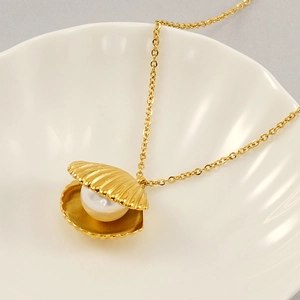 Elegant gold shell necklace with a single white pearl centerpiece in a ceramic shell dish