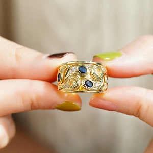 Détail macro d'une bague large dorée avec pierres bleues et jaunes et pavé scintillant