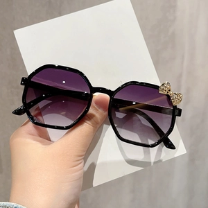 Detail of children's sunglasses with purple gradient lenses and gold metal bow decoration